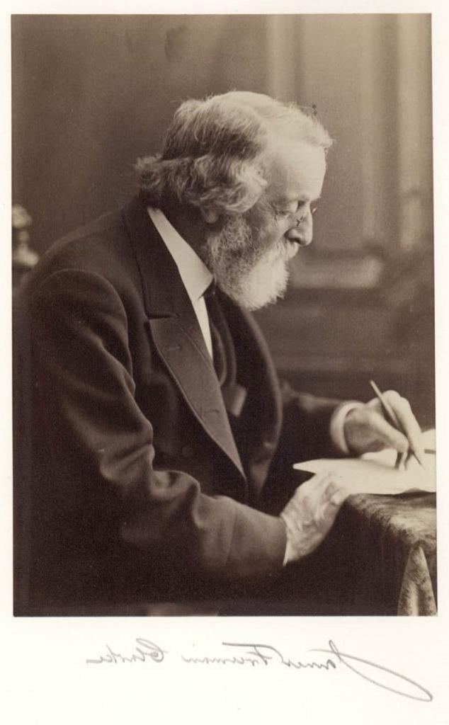 Black-and-white photograph of a white man with gray hair, beard, and glasses seated at a desk writing. Below the photograph is the signature “James Freeman Clarke.” 